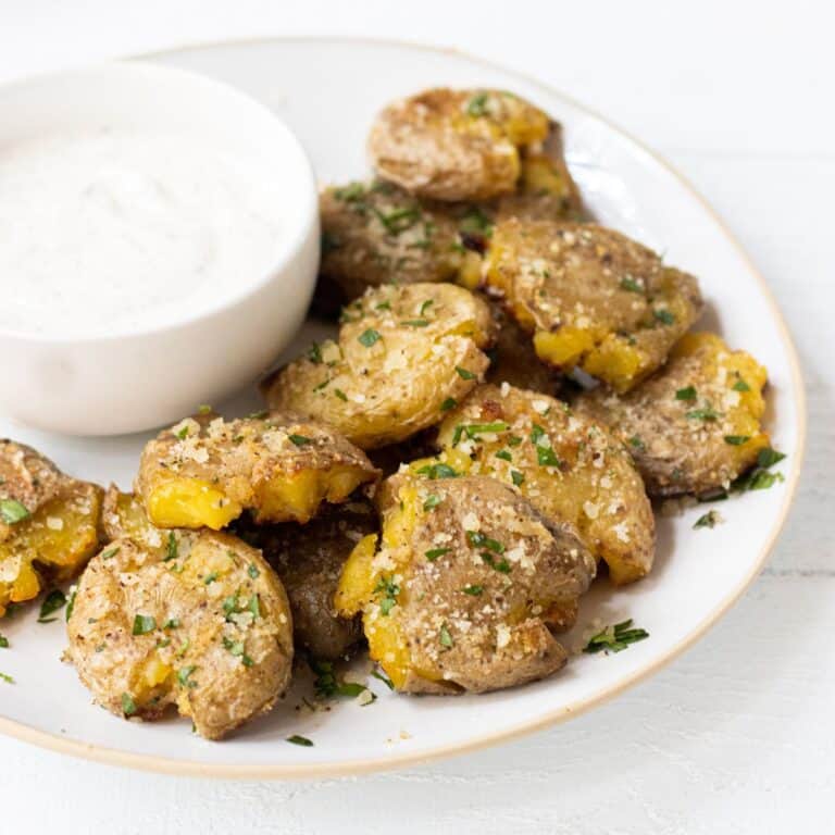 Smashed fingerling potatoes on a plate with a bowl of ranch.