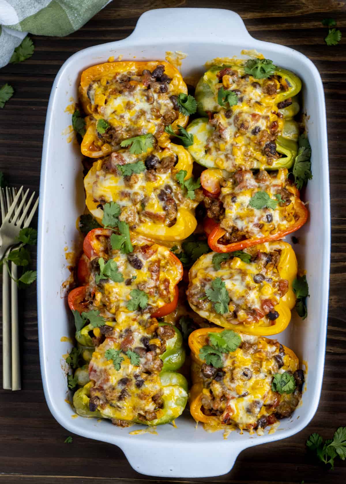 Eight taco stuffed peppers in a baking dish next to forks and a towel.