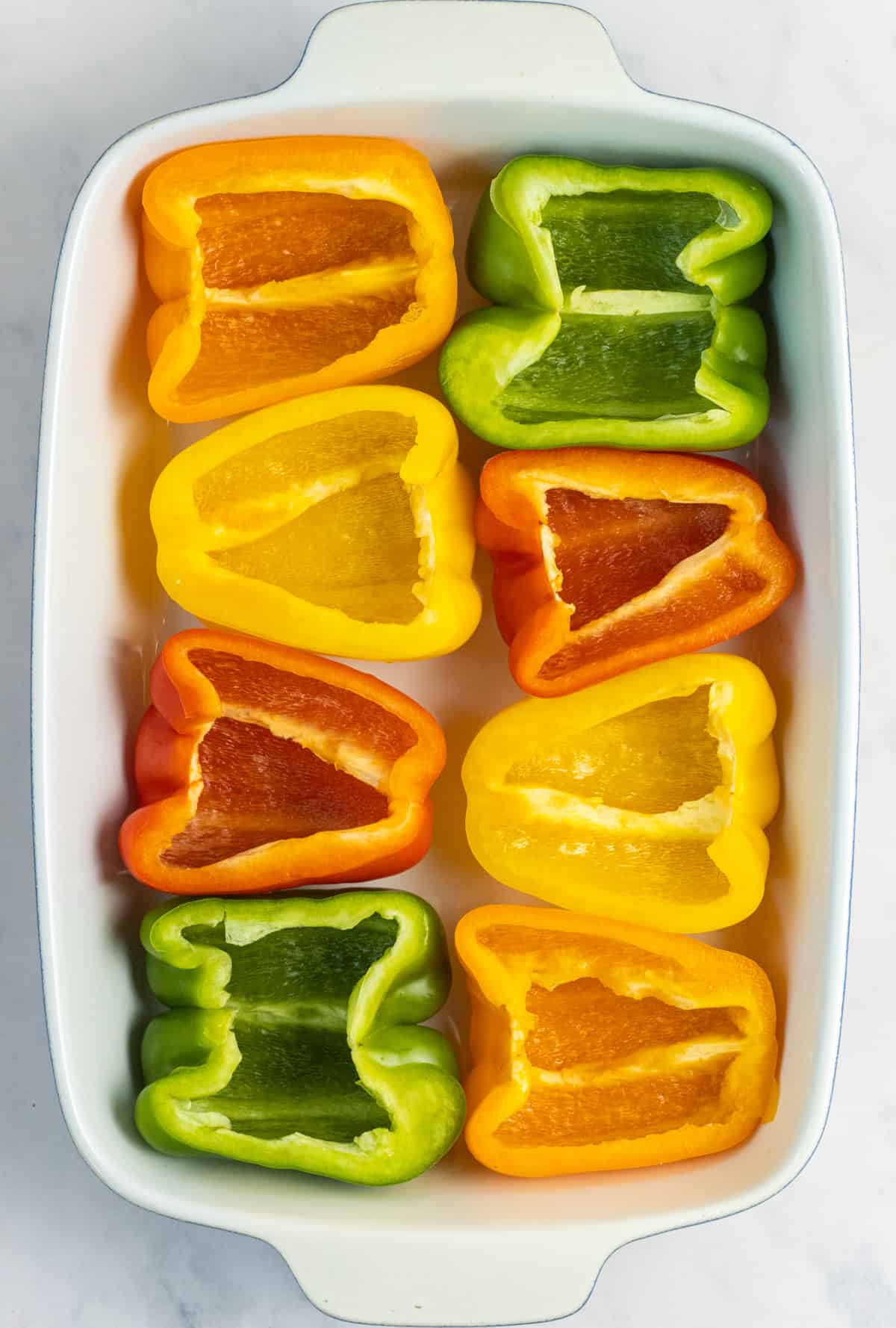 Bell peppers of a variety of colors cut in half with the cut side up in a baking dish.
