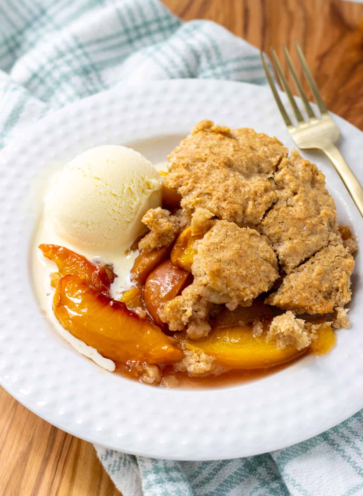 Peach cobbler on a plate with a scoop of vanilla ice cream and a fork.