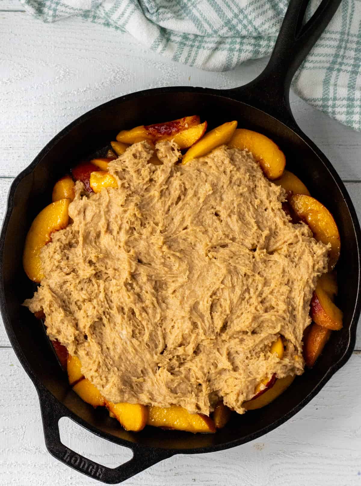 Unbaked peach cobbler in a cast iron pan.