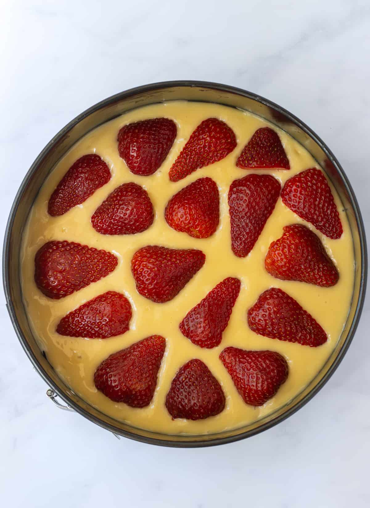Vanilla cake batter topped with strawberry halves.