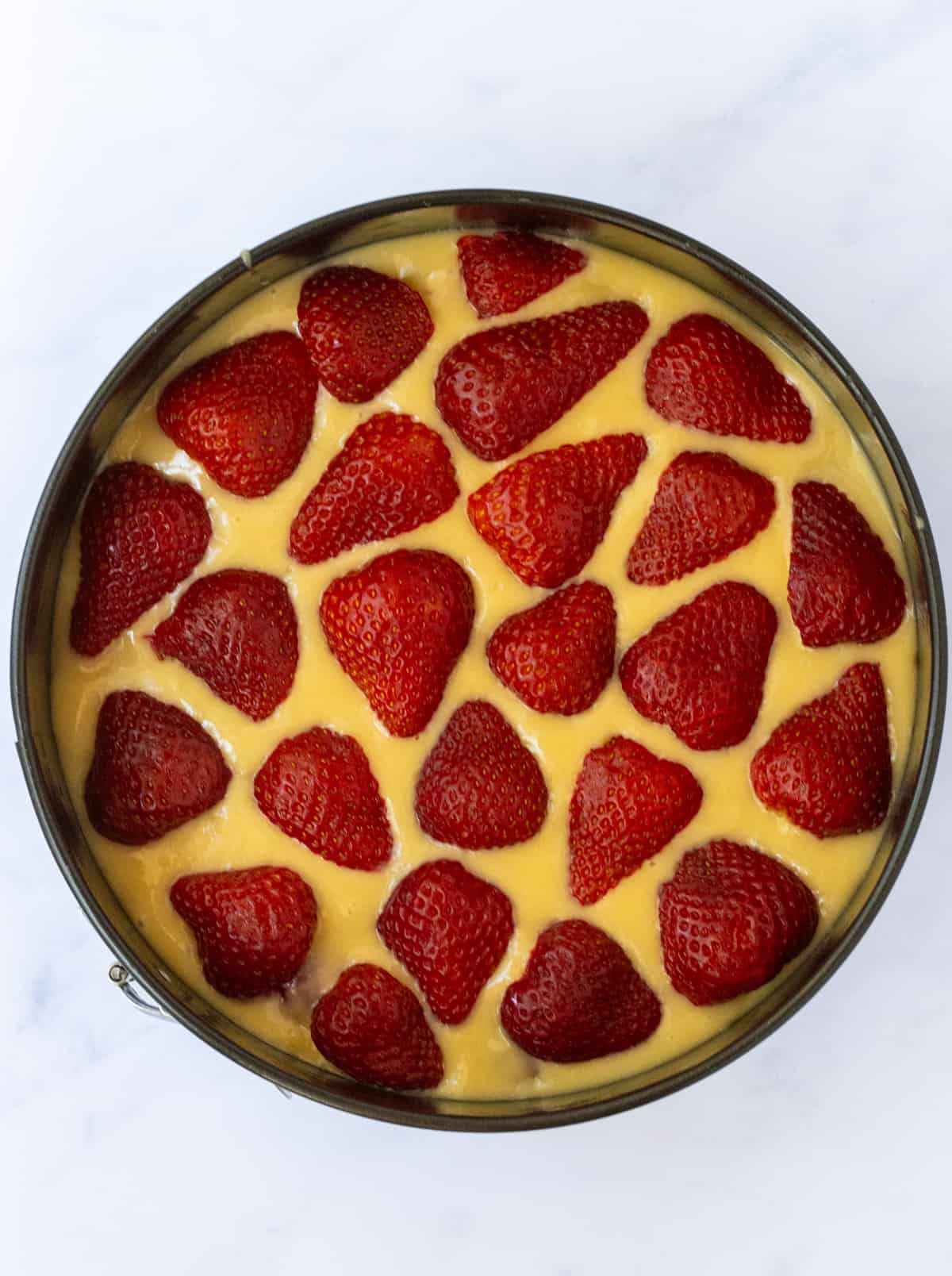 Vanilla cake batter topped with strawberry halves in a springform pan.