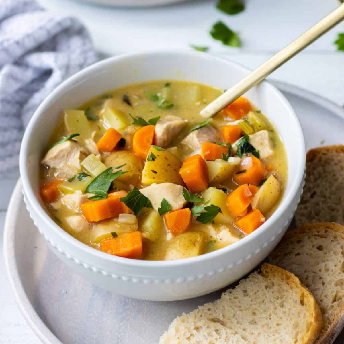 Bowl of chicken stew on a plate with slices of crusty bread.