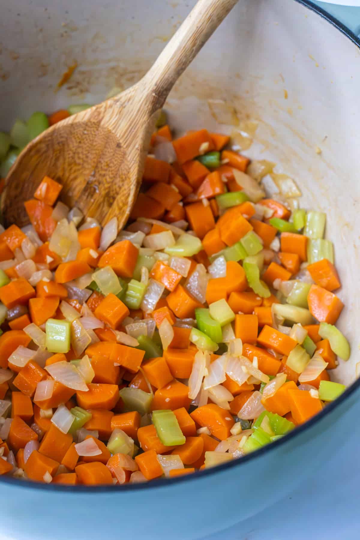 Diced carrots, onion, celery, and garlic in a pot with a wood spoon.