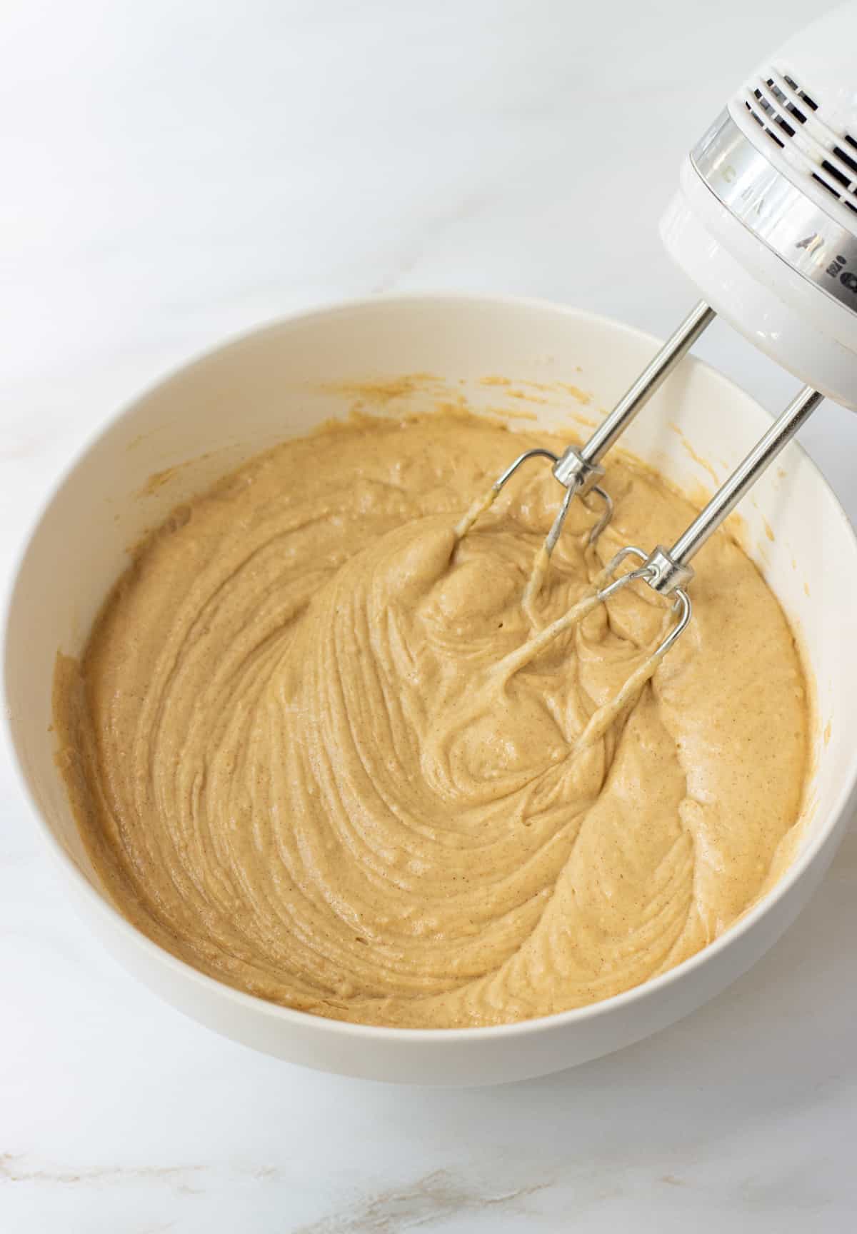 Cinnamon muffin batter in a bowl with beaters.