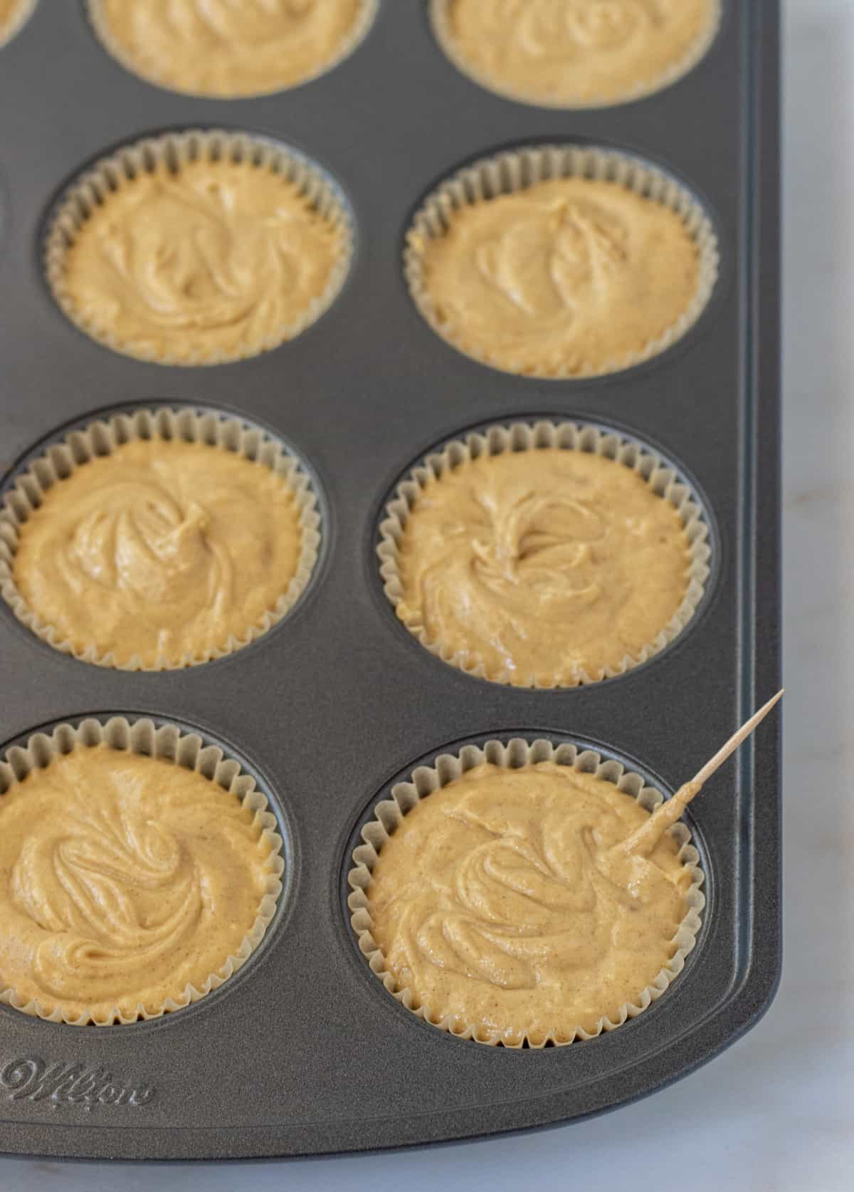 Muffin liners filled with muffin batter and one with a toothpick sticking out.