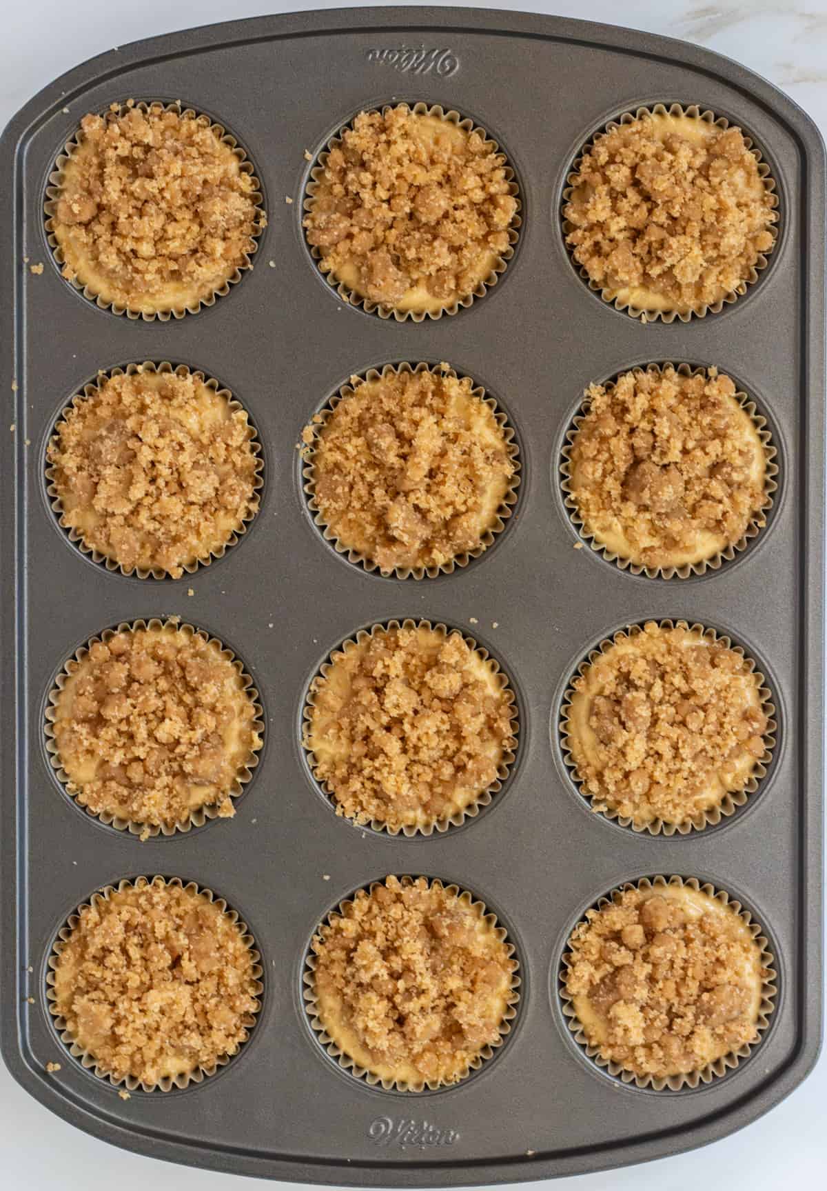 Unbaked streusel topped muffins in a muffin pan.