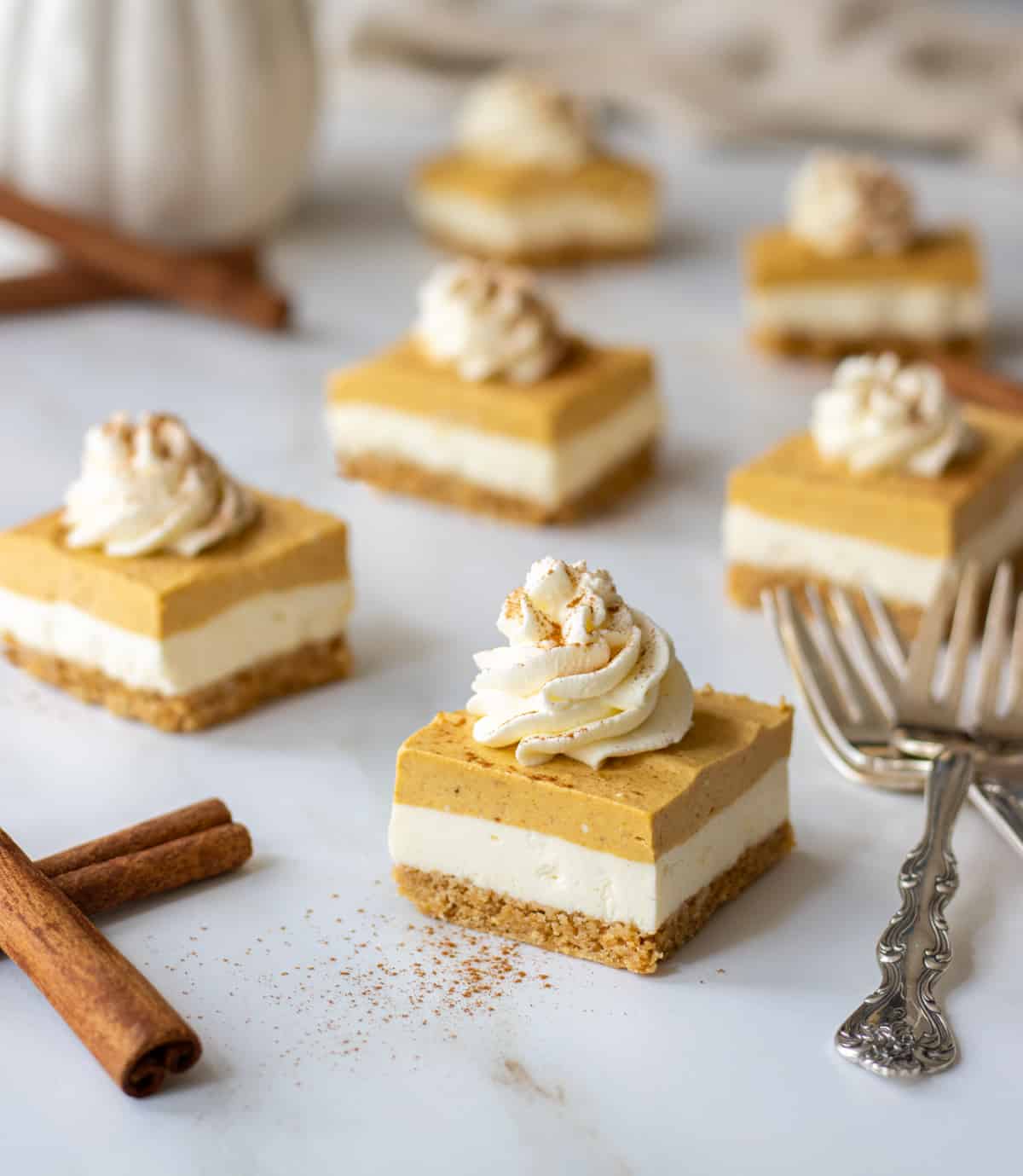 Pumpkin cheesecake bars topped with cream cheese and cinnamon with cinnamon sticks and forks next to them.