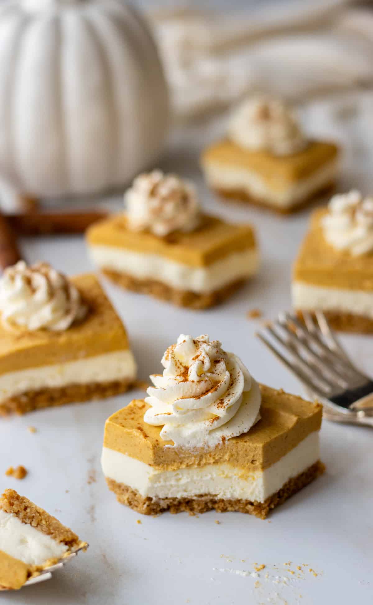 Pumpkin cheesecake bars on a table with forks and a ceramic pumpkin.