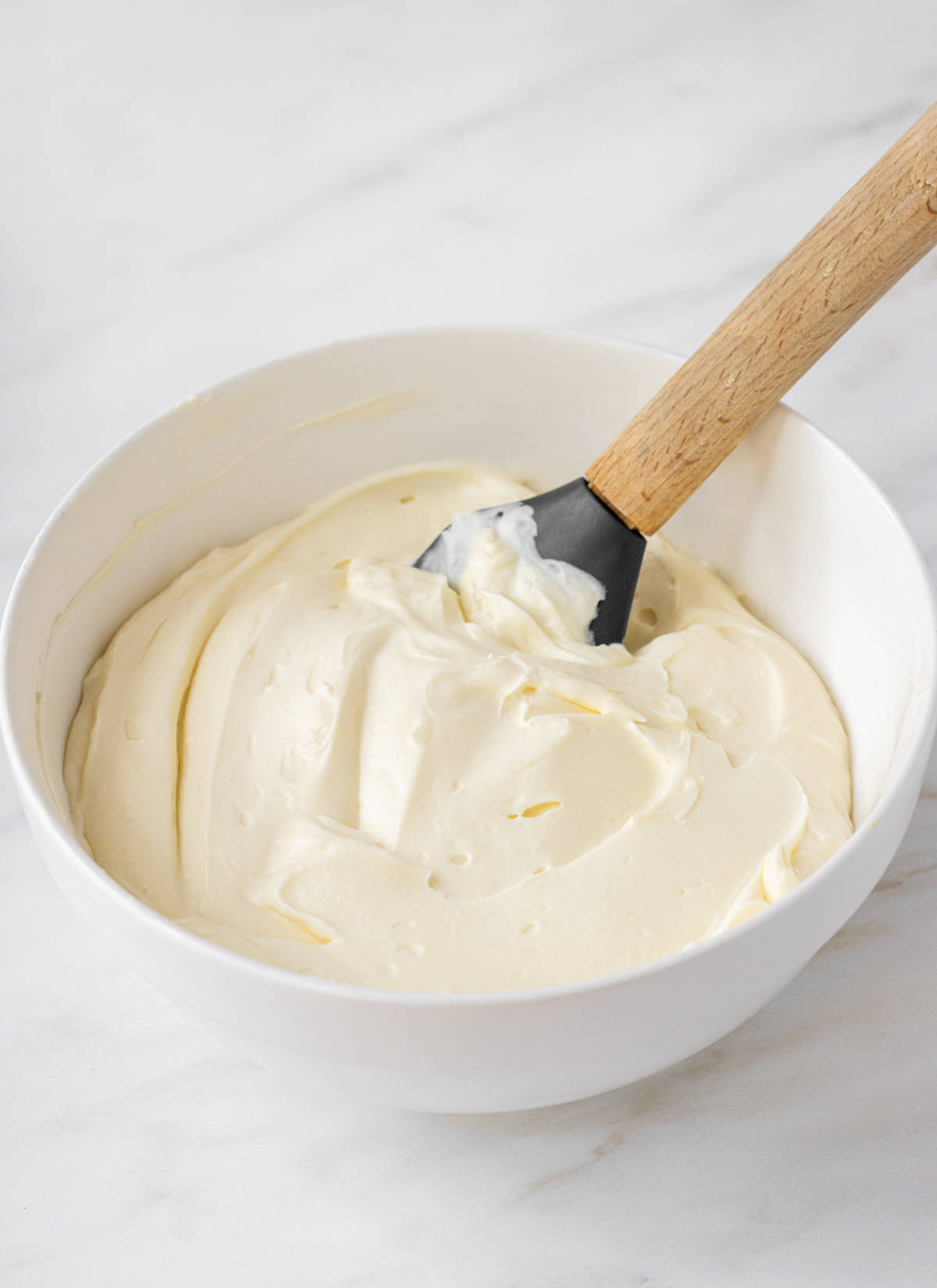 Vanilla cheesecake mixture in a bowl with rubber spatula.