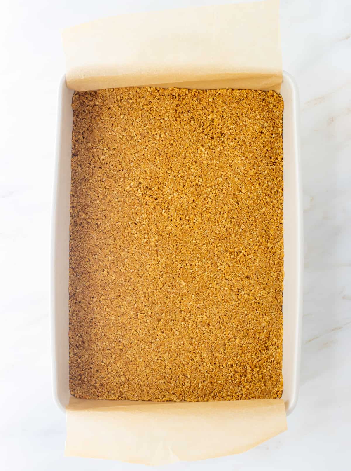 Graham cracker crust pressed into a parchment lined baking dish.