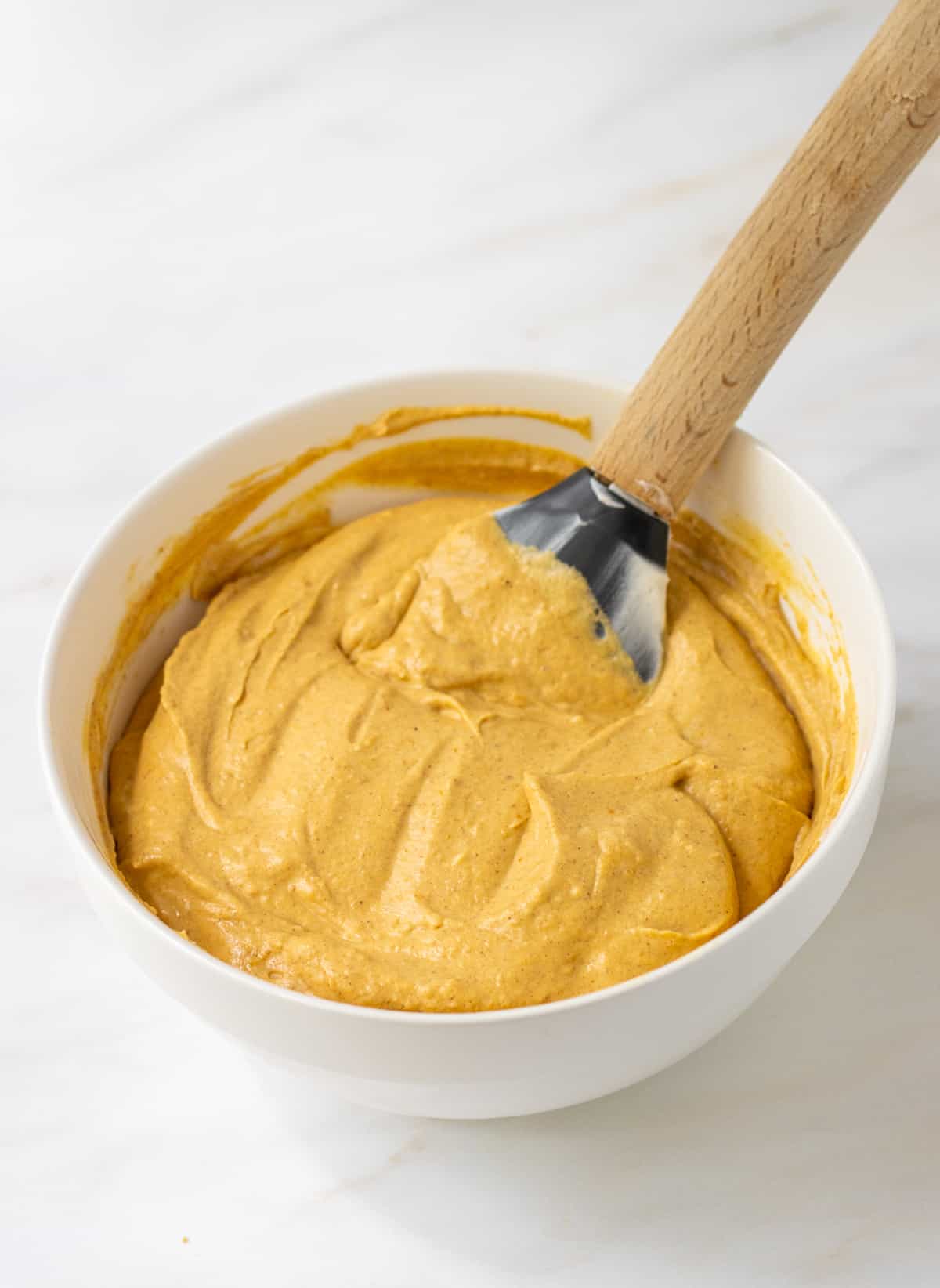 Pumpkin cheesecake mixture in a bowl with a rubber spatula.