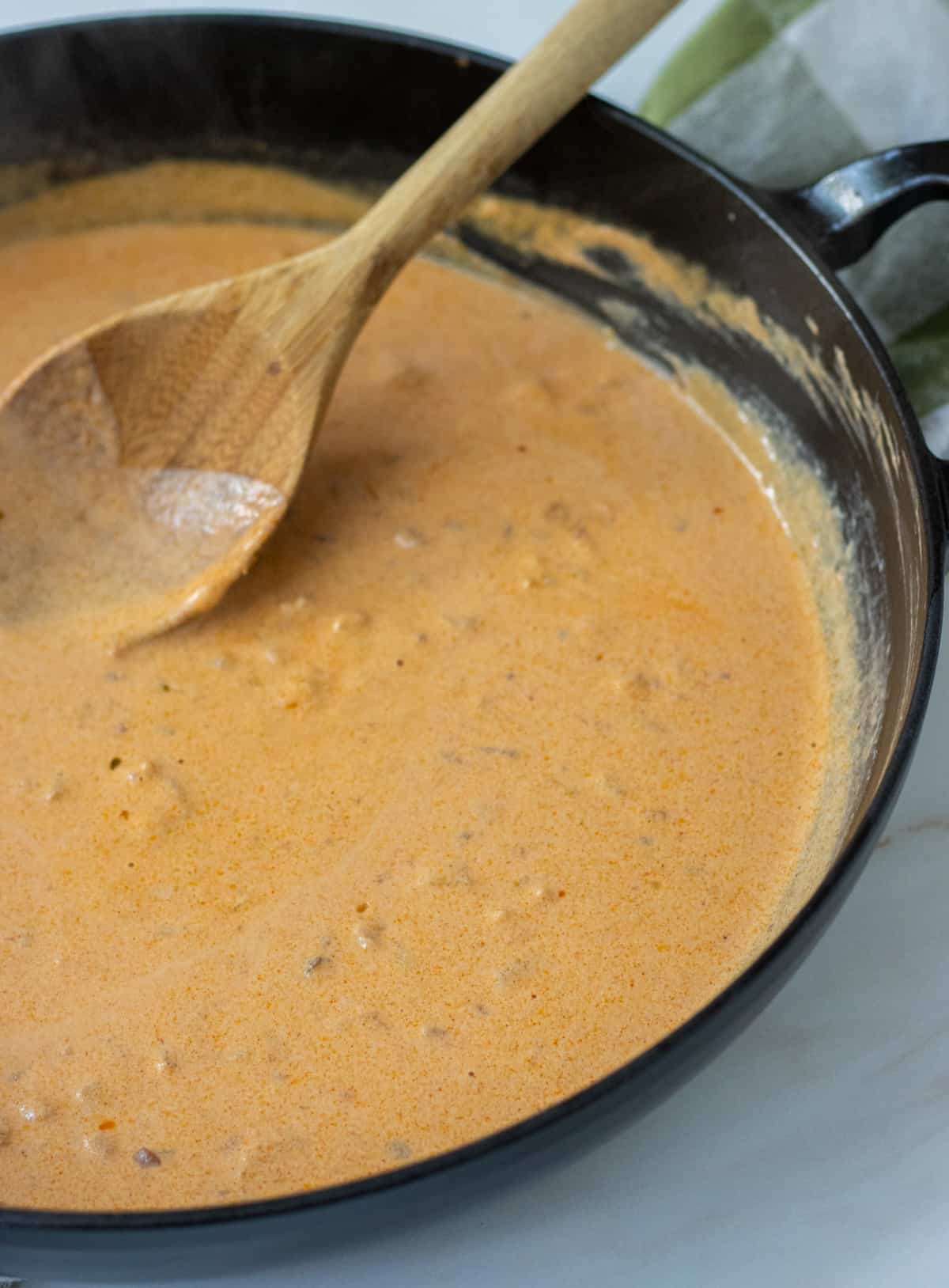 Creamy tomato sauce in a skillet with a wood spoon.