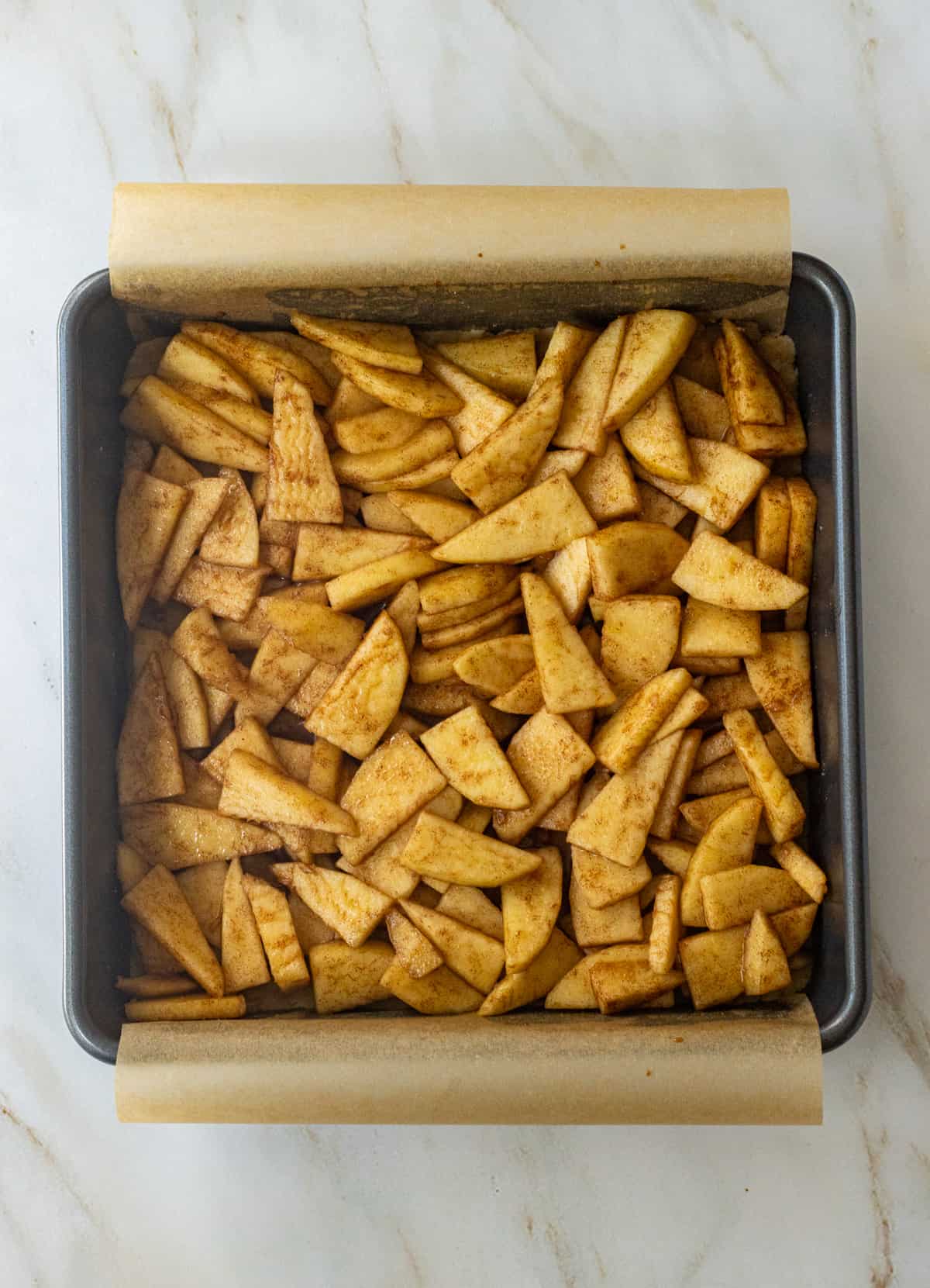 Cinnamon apple slices in a parchment lined baking dish.
