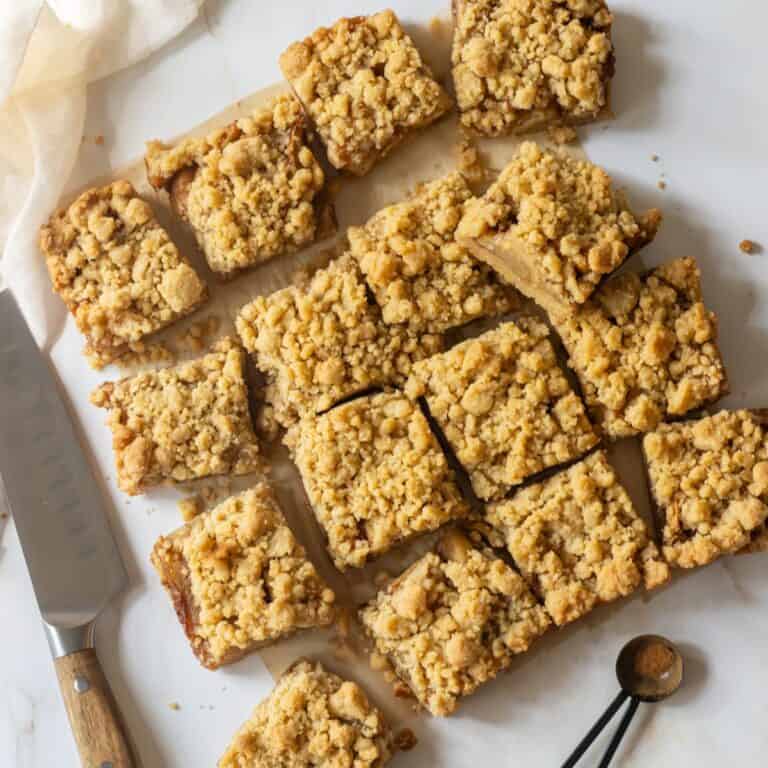 Apple bars on a table next to a knife and a measuring spoon with cinnamon in it.