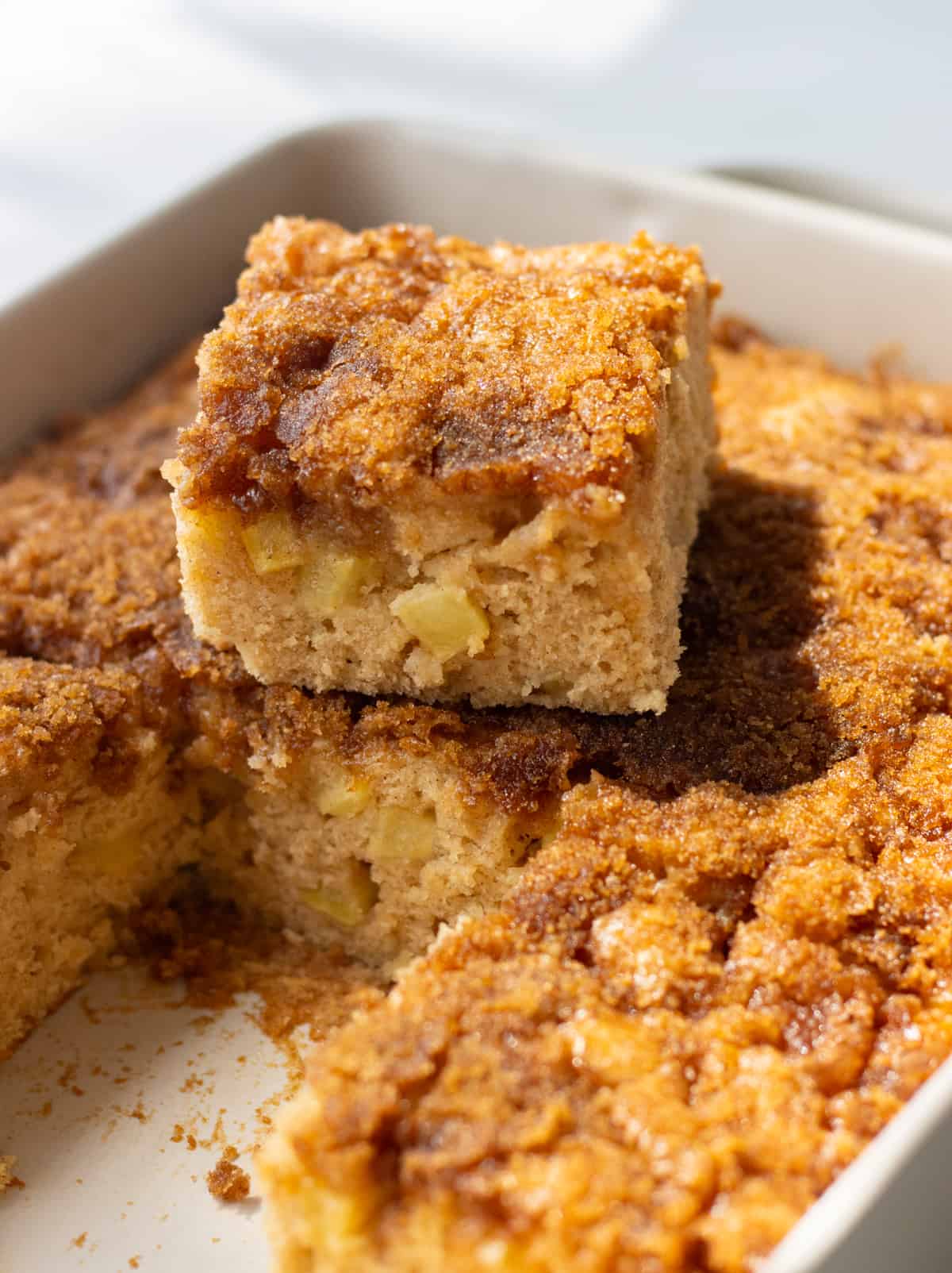 Cinnamon apple cake sliced up in a baking dish with one slice stacked on another.