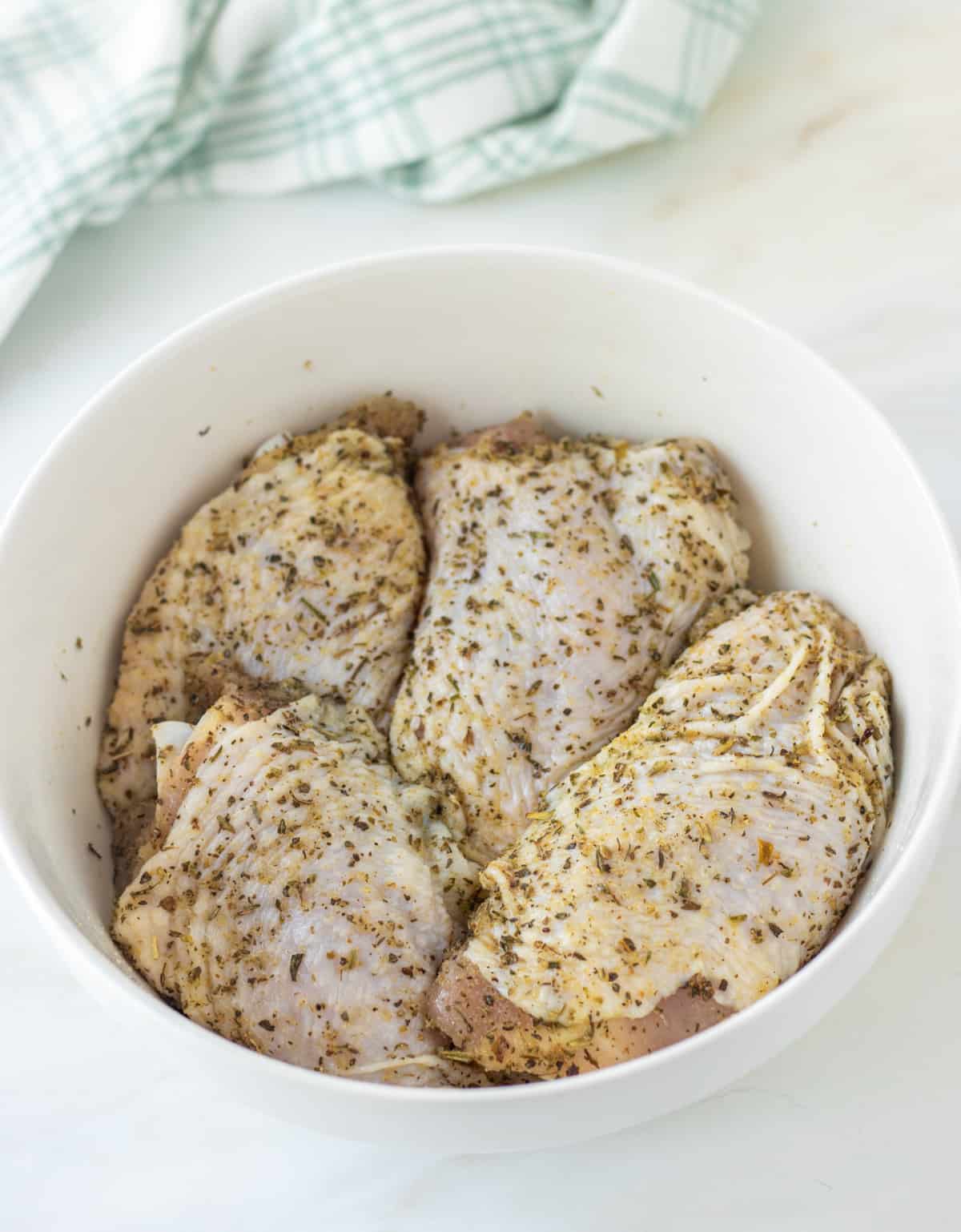 Chicken thighs in a bowl tossed with herbs.
