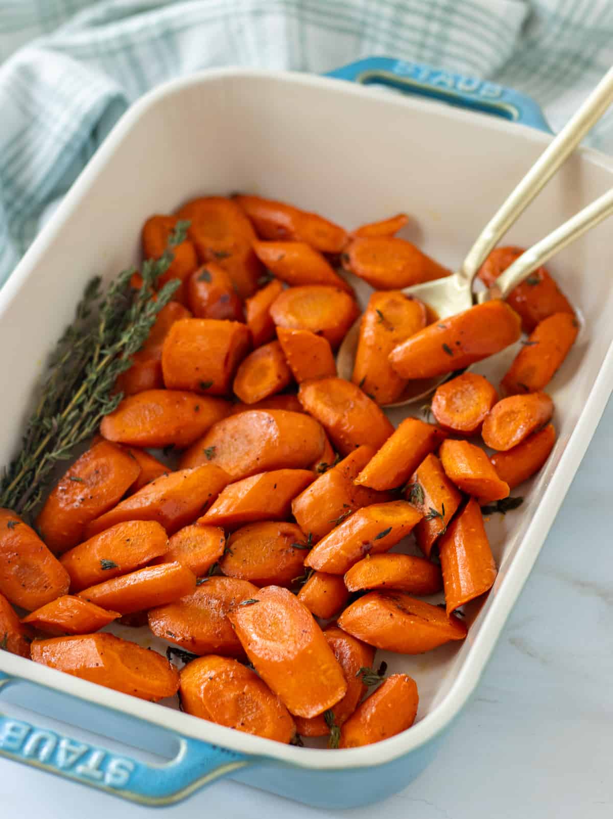 Roasted carrot slices in a baking dish with two large spoons and fresh thyme.