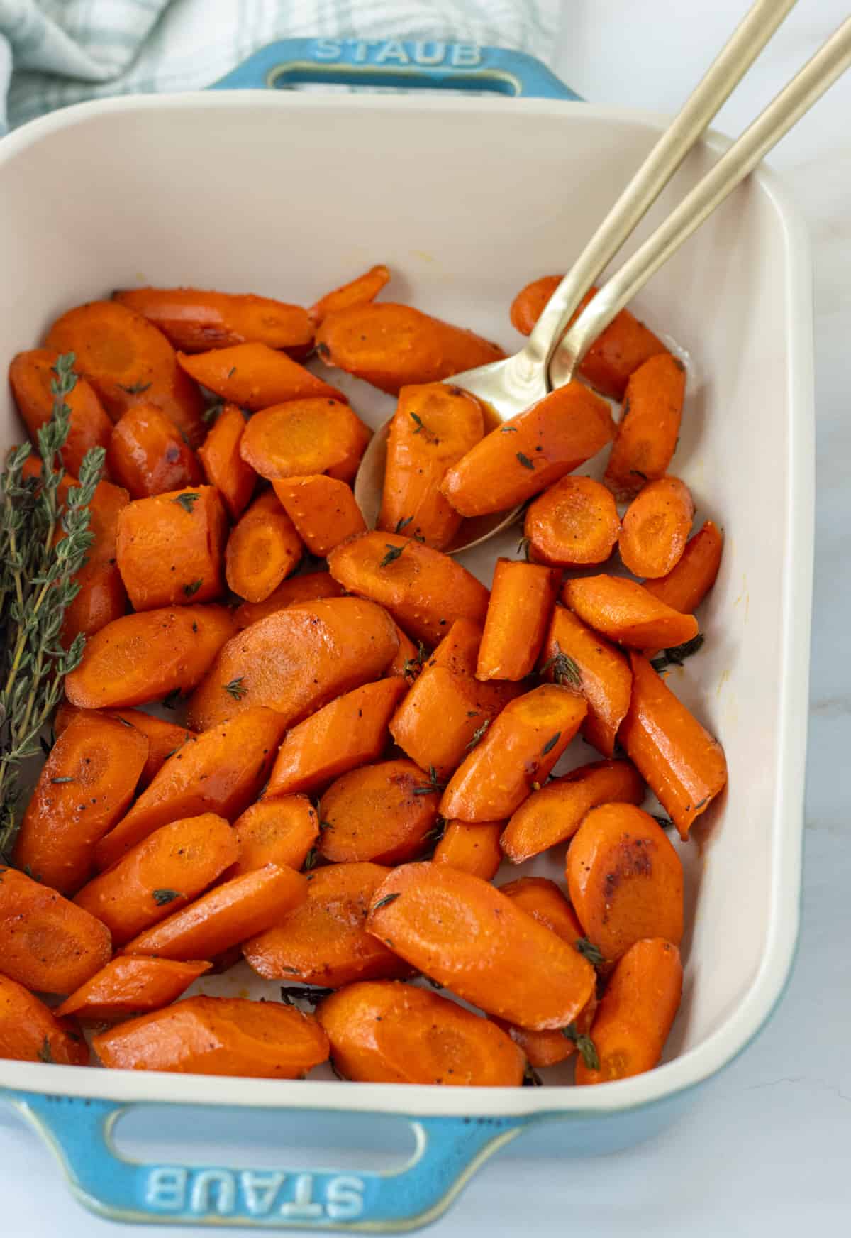Honey thyme roasted carrots in a serving dish with two spoons and fresh thyme.