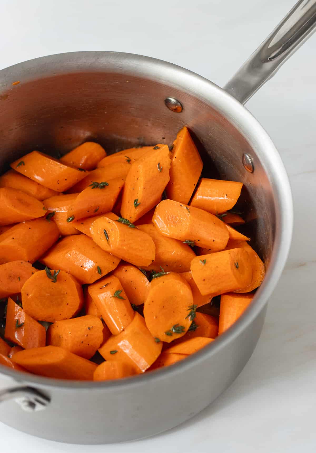 Carrots tossed in honey thyme sauce in a saucepan.