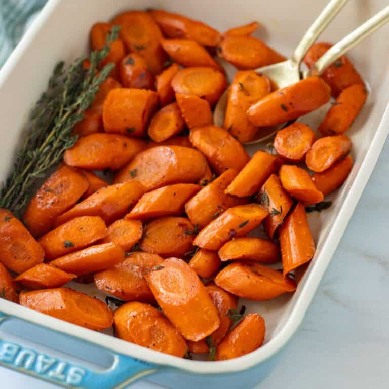Roasted carrot slices in a baking dish with two large spoons and fresh thyme.