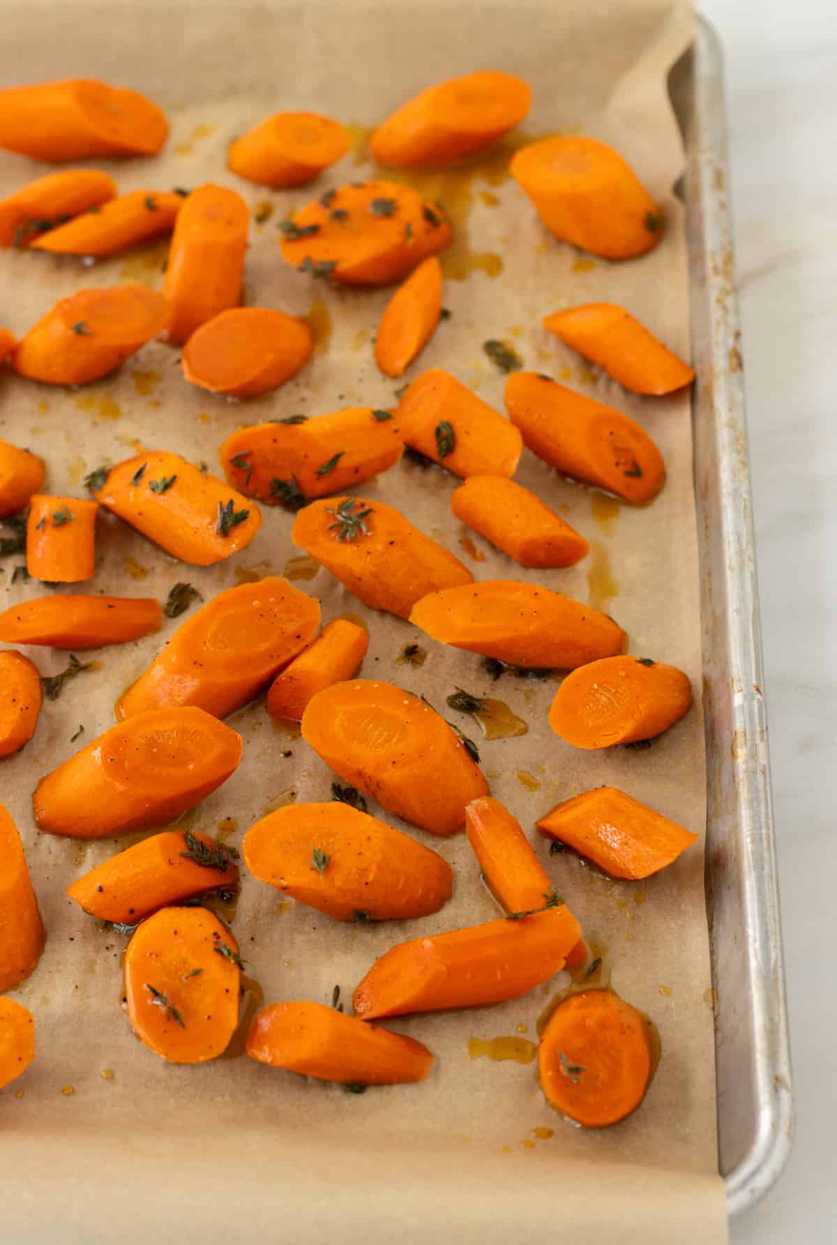 Carrots slices in a honey thyme sauce on a parchment lined baking sheet.