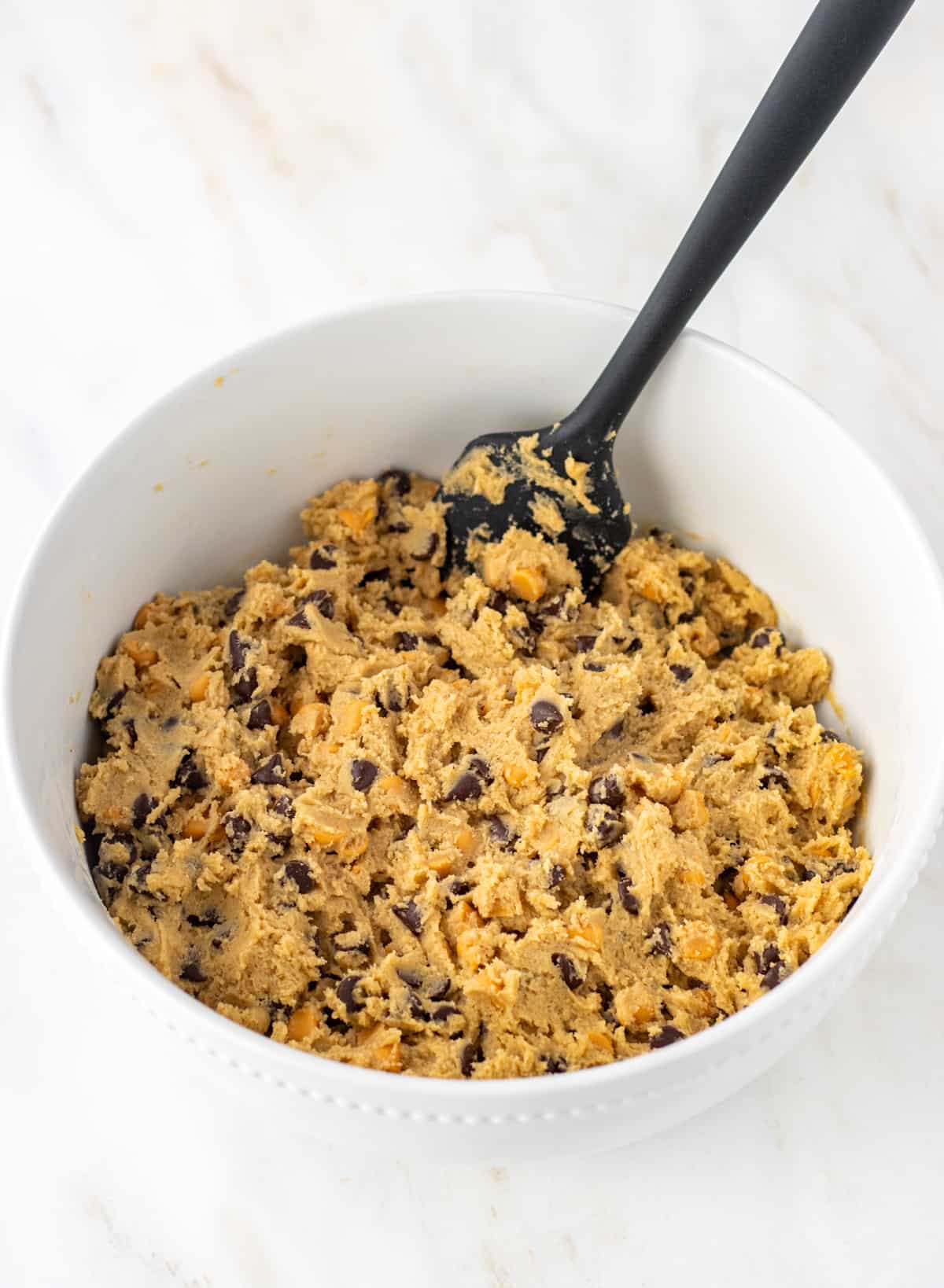 Butterscotch chocolate chip cookie dough in a bowl with a rubber spatula.