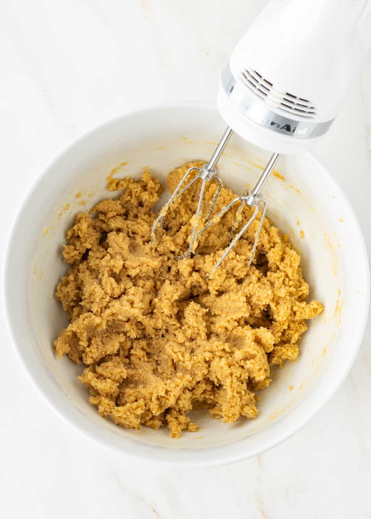 Butter, brown sugar, and white sugar creamed together in a bowl with a hand mixer on the side.