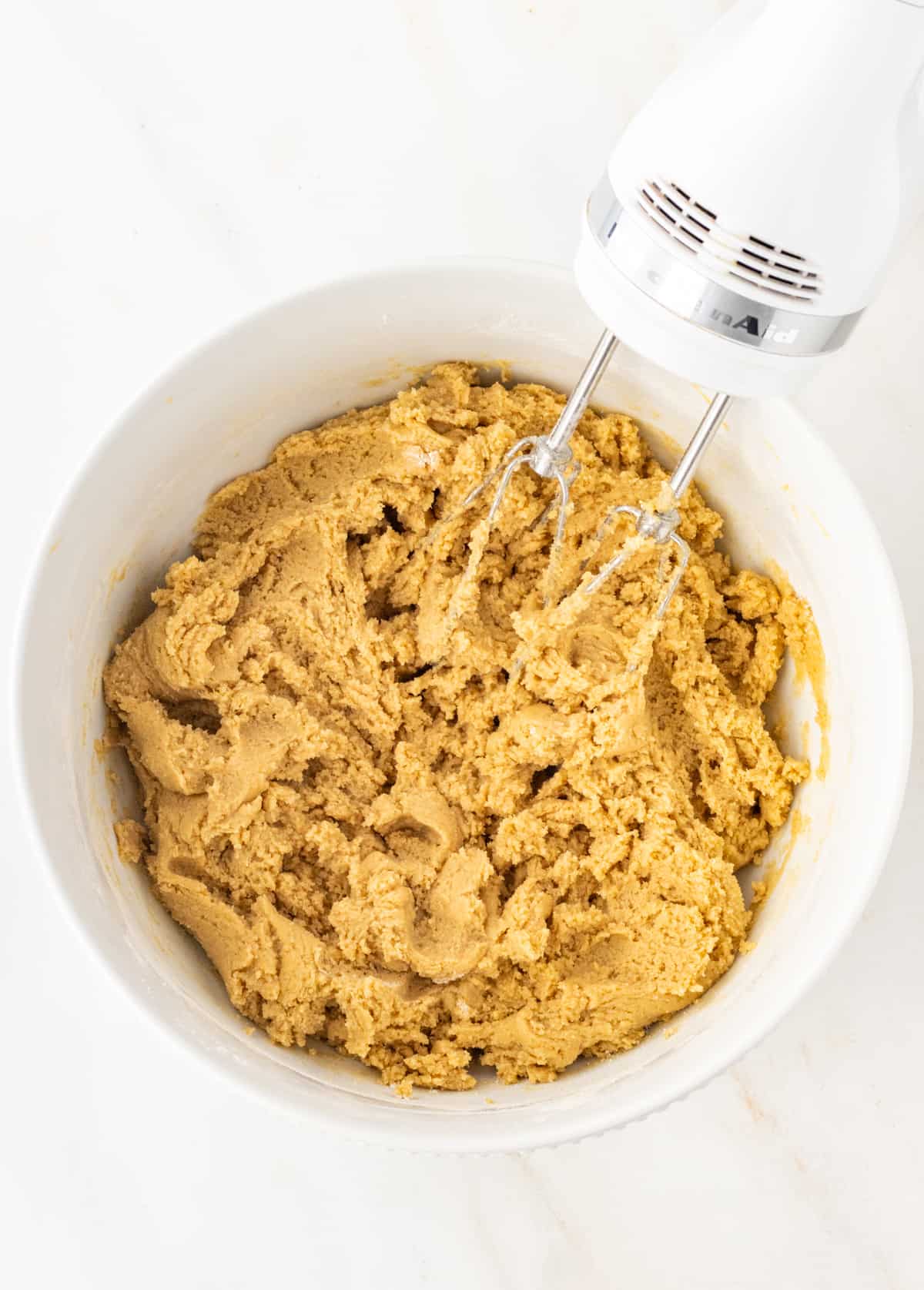 Cookie dough in a bowl with an electric whisk before adding the butterscotch and chocolate chips.