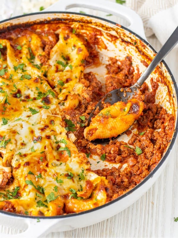 Stuffed shells in a meat sauce in a casserole dish with a large spoon.