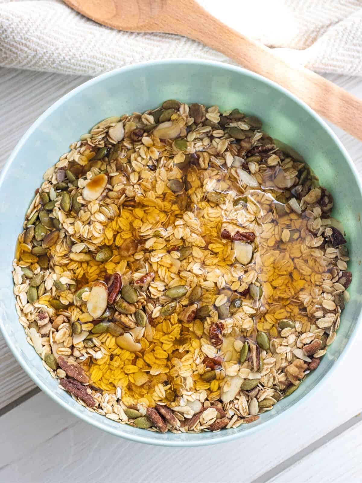 Honey, vanilla, and oil on top of oats, pumpkin seeds, and nuts in a bowl.