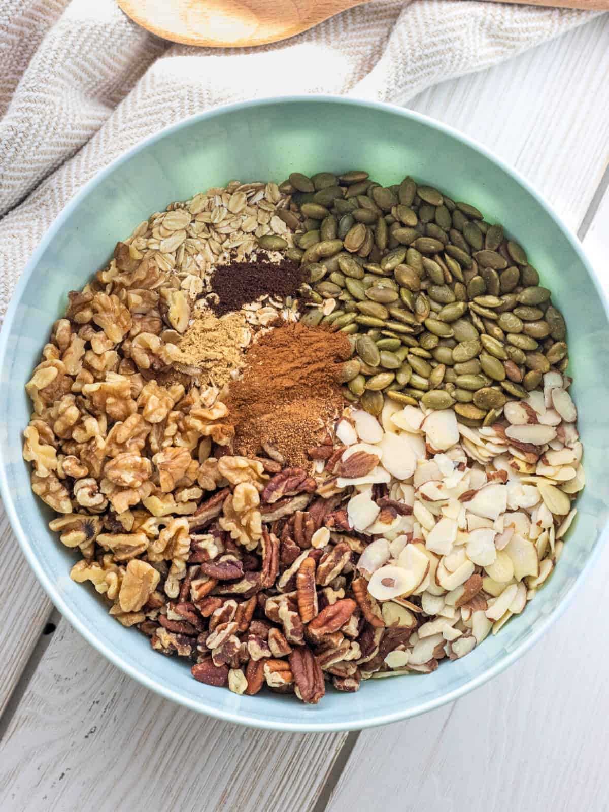 Spices on top of oats, pumpkin seeds, and nuts in a bowl.