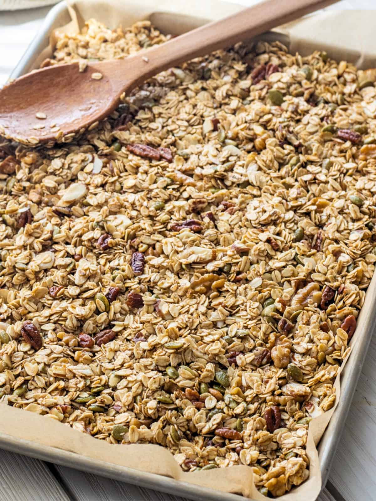 Granola mixture spread out on a baking sheet with a wooden spoon.