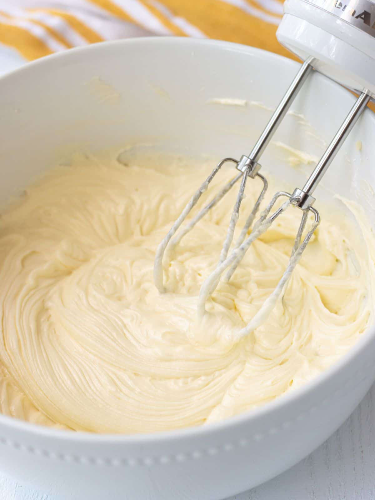Cream cheese frosting in a bowl with an electric whisk.
