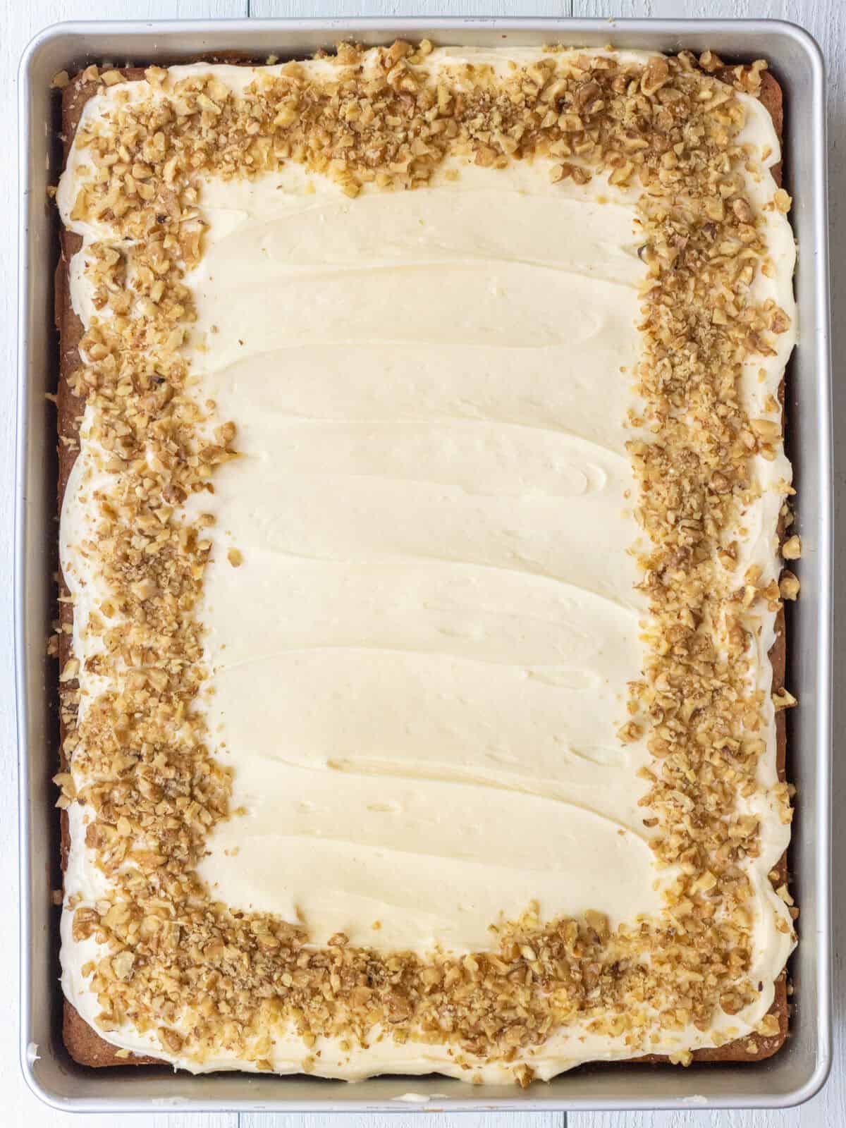 Chopped walnuts around the edges of banana cake topped with cream cheese frosting.