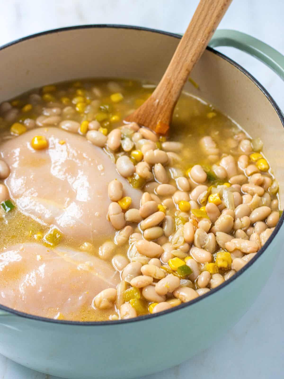 Broth, chicken, and beans added to a Dutch oven with a wood spoon.
