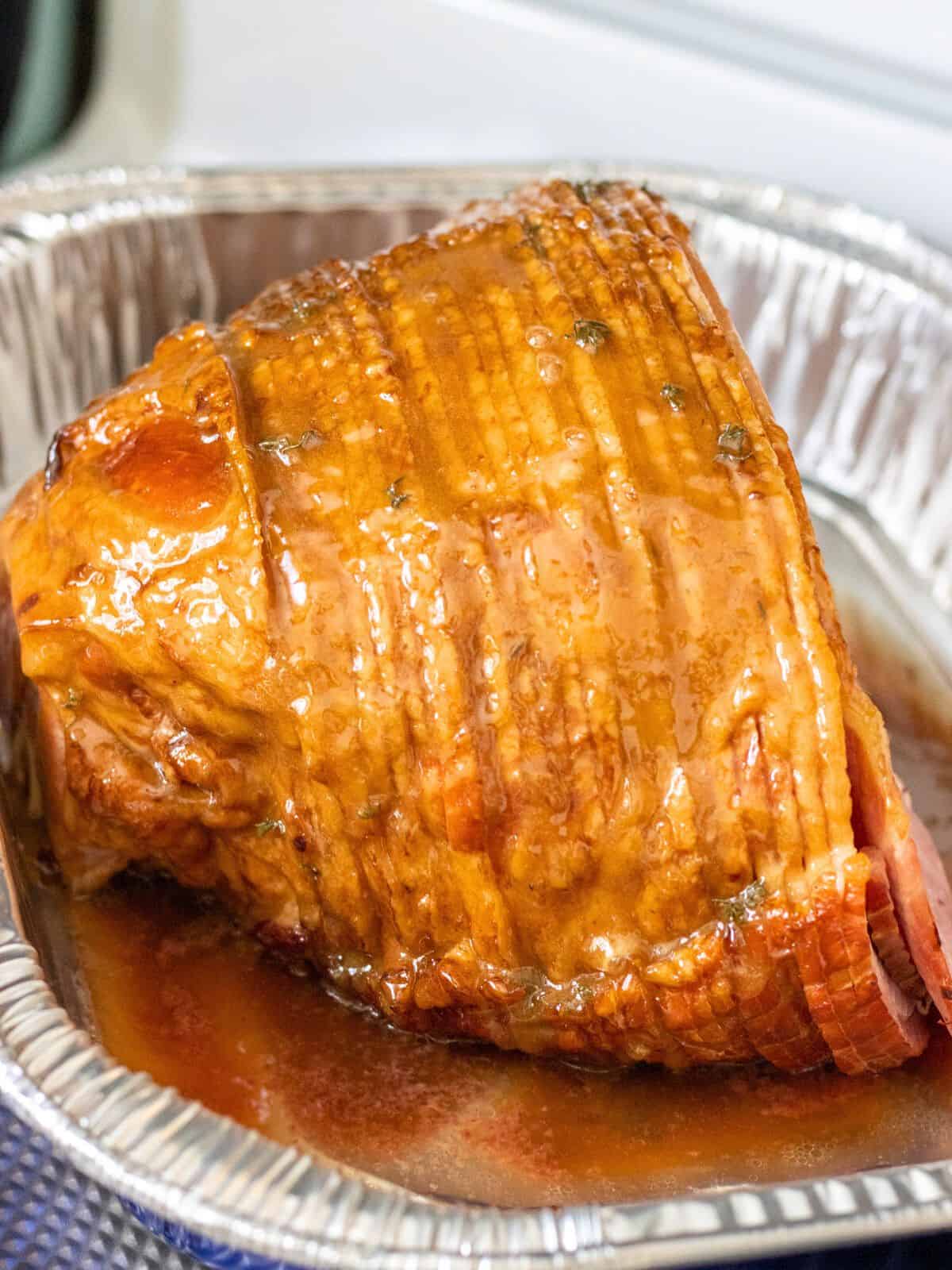 Spiral ham covered in honey glaze in a foil tin.