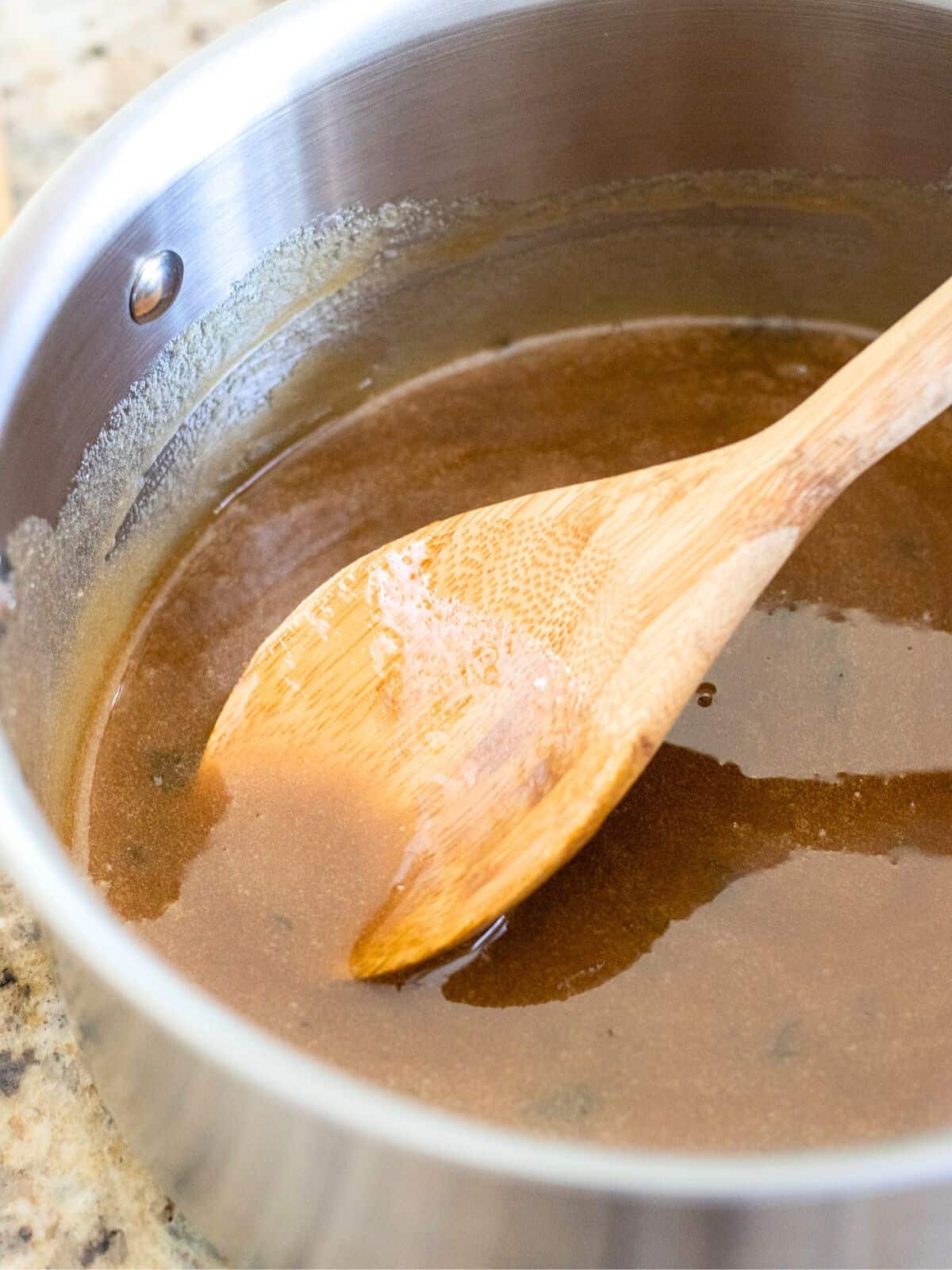 Honey glaze in a sauce pan with a wood spoon.