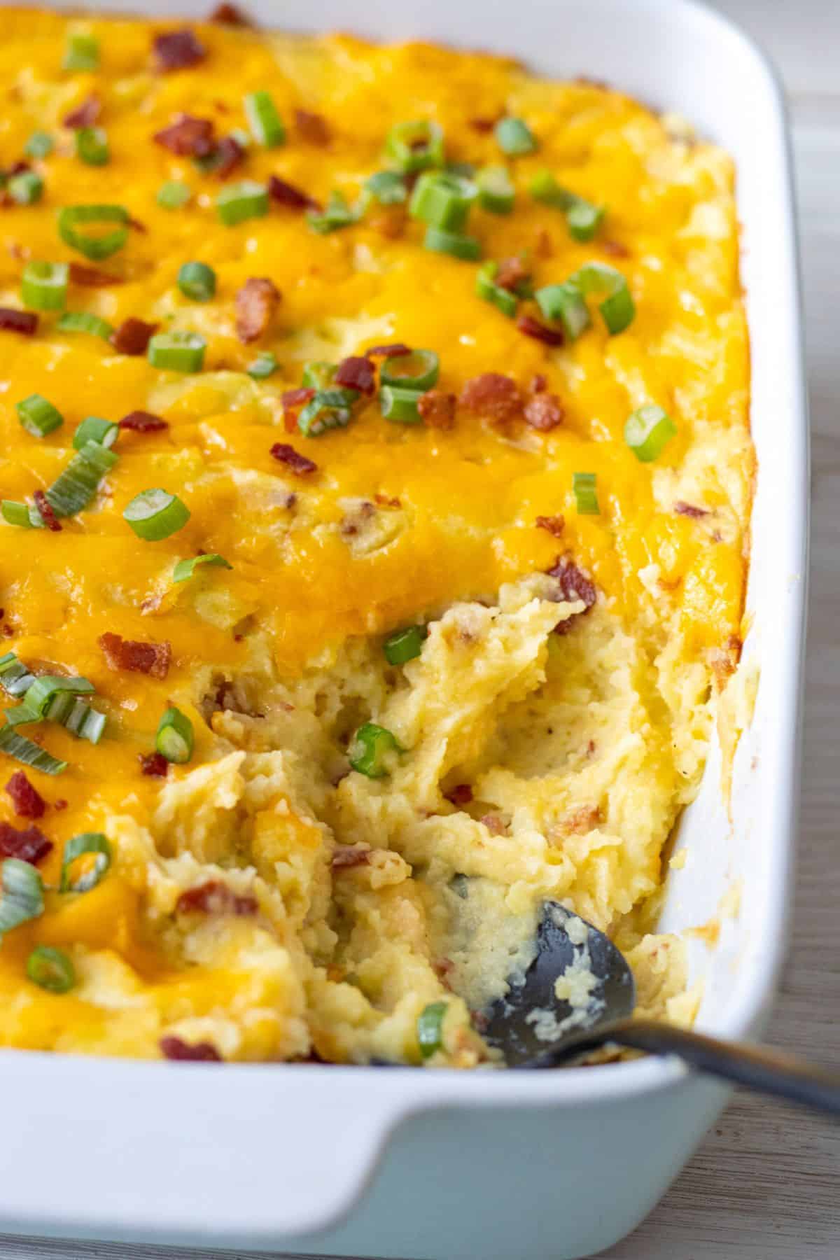 Baking dish filled with loaded mashed potatoes with a scoop taken out. 