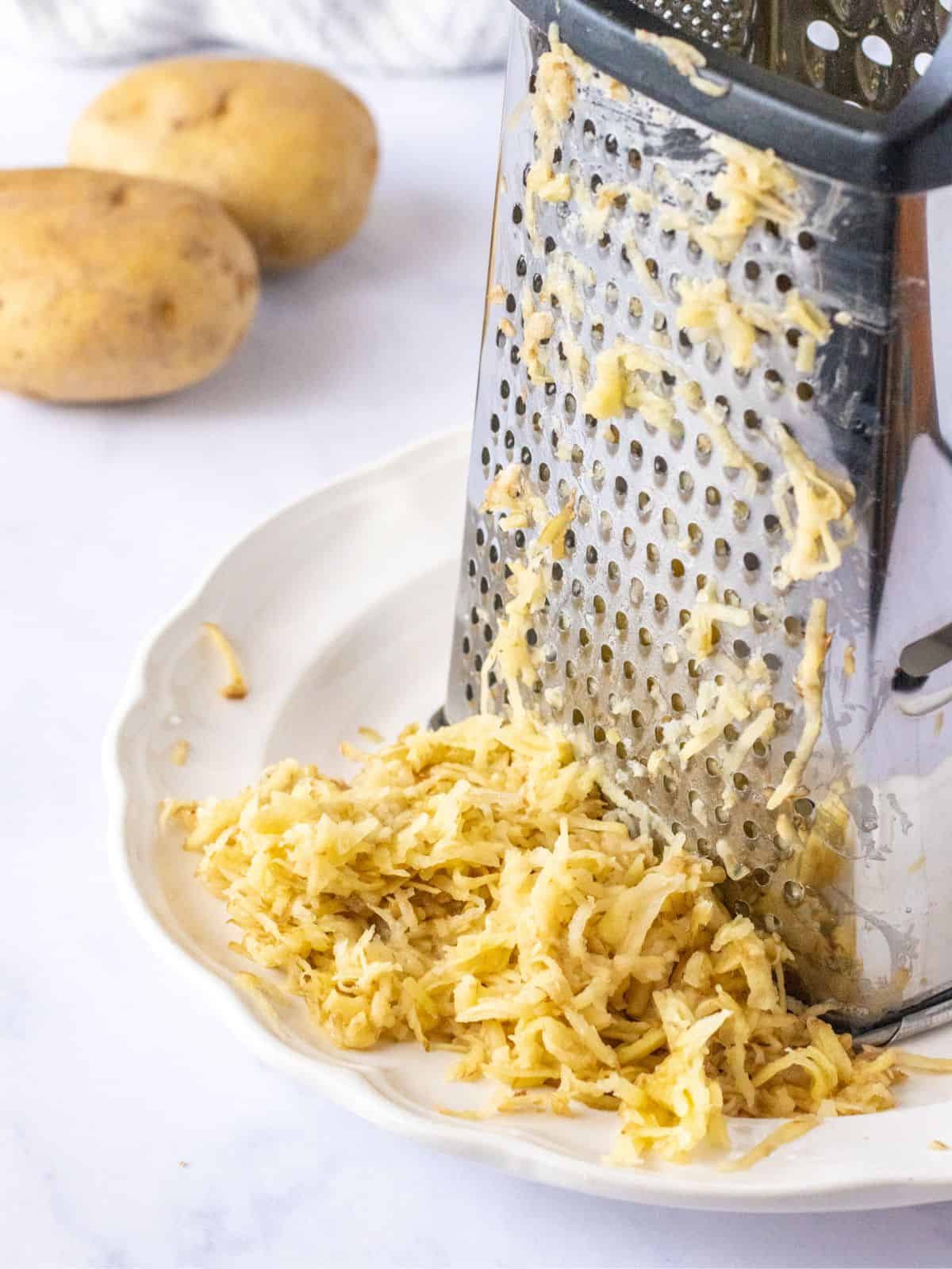 Grated potatoes on a plate next to a box grater.