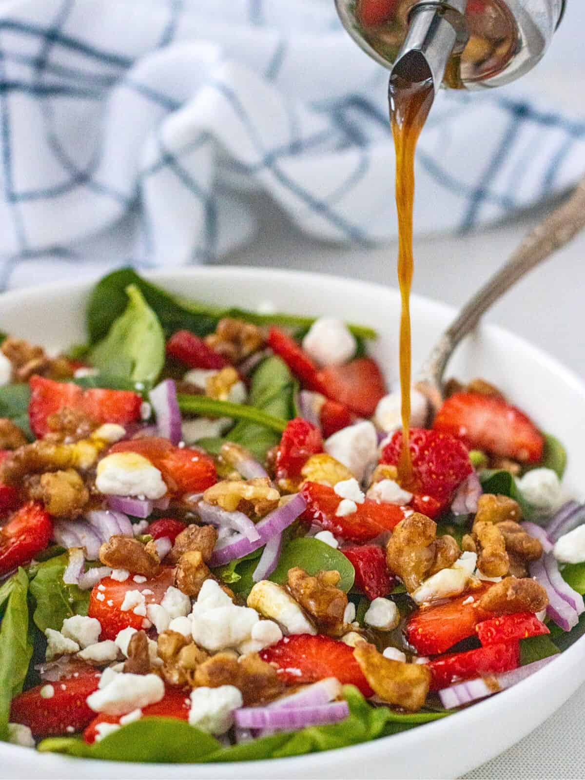 Balsamic dressing being poured over strawberry goat cheese salad.