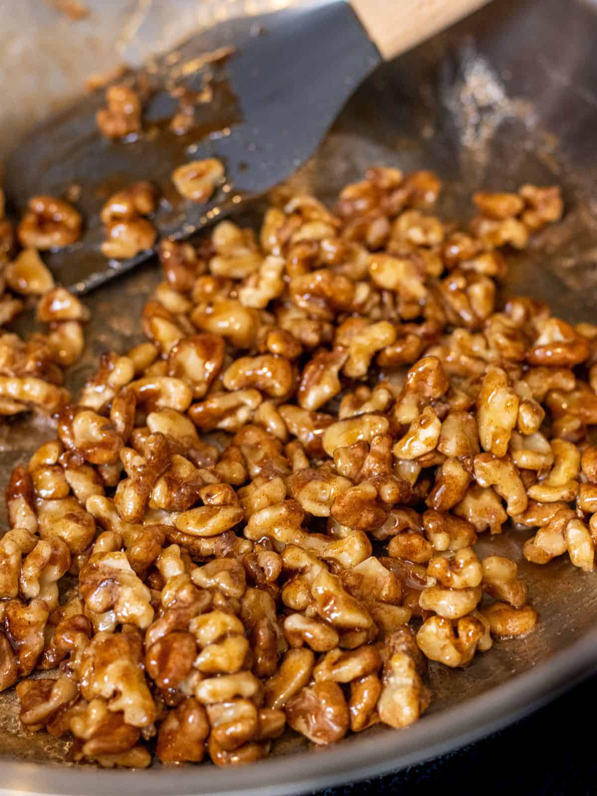 Walnuts tossed in brown sugar sauce in a skillet with a spatula.