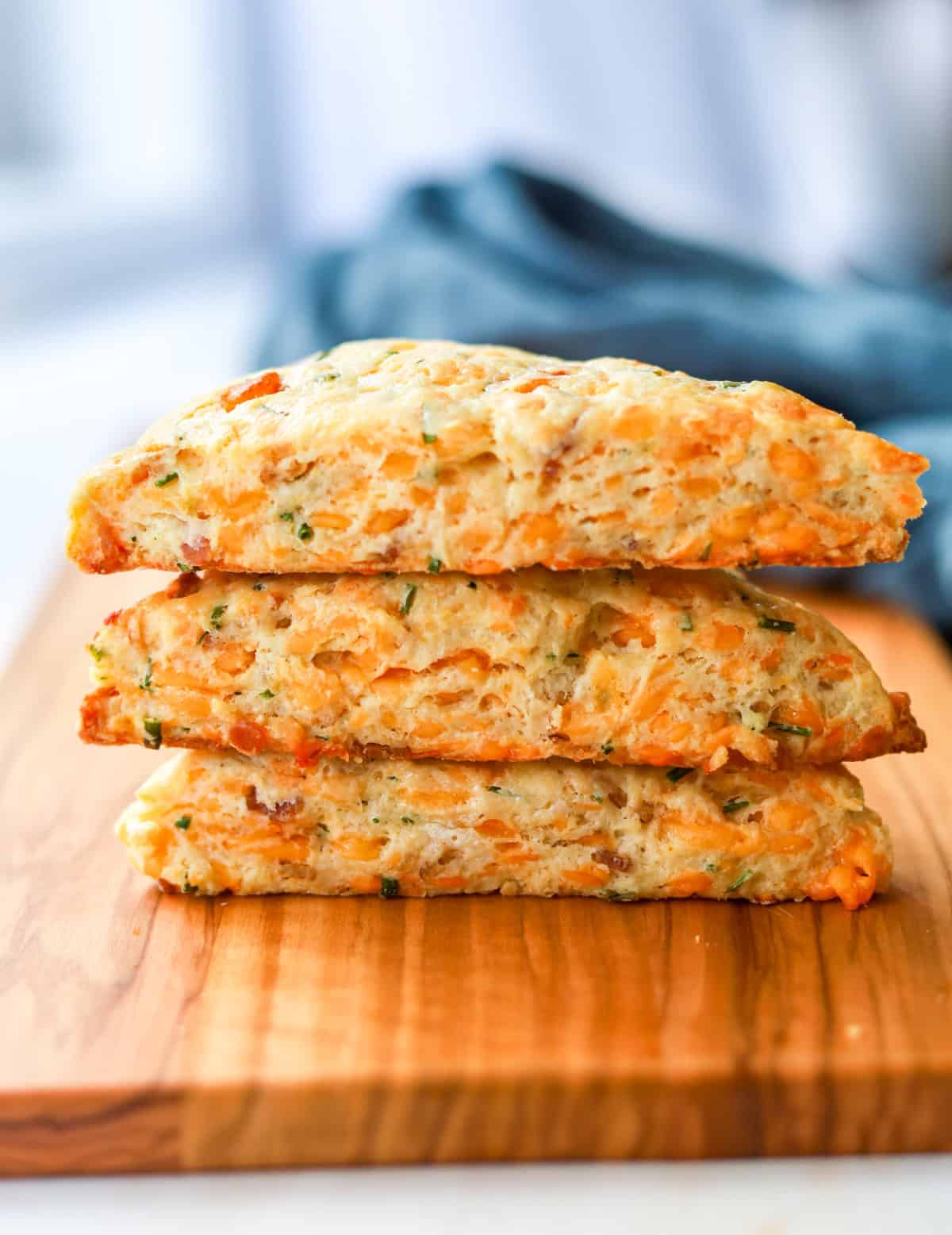 Three bacon cheddar chive scones stacked on top of each other on a board.